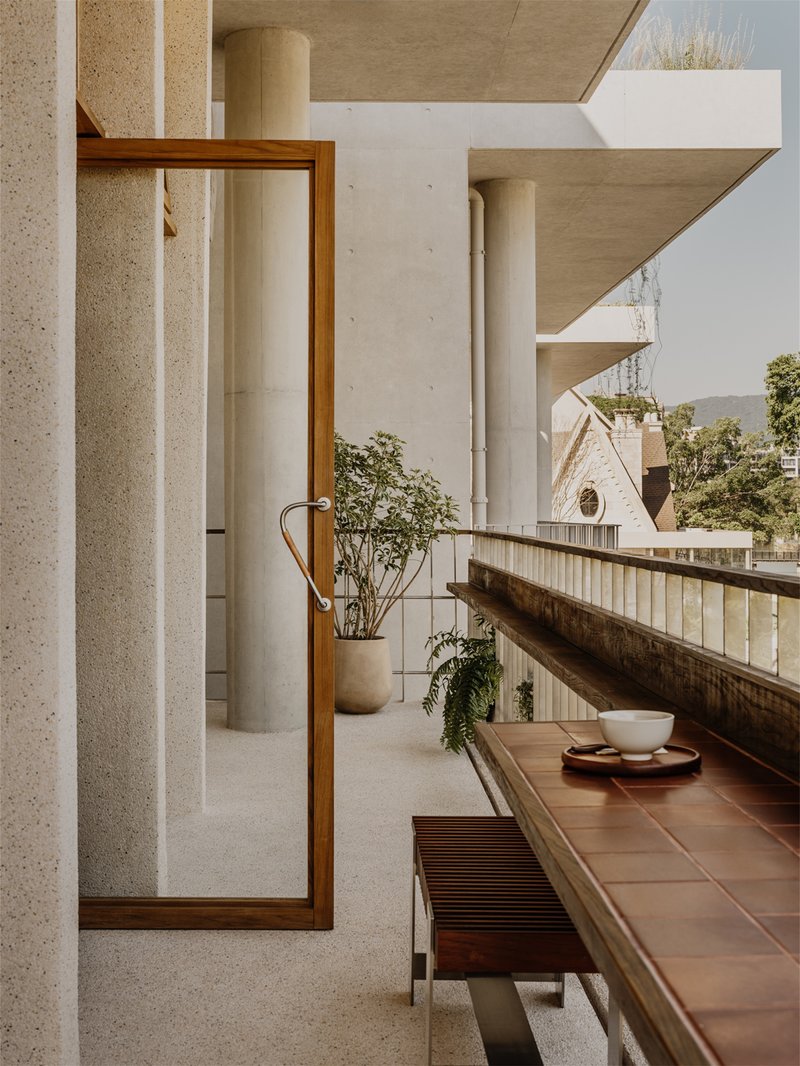 Covered terrace with cylindrical concrete columns, timber-framed mirror, and potted plants on tiled ledge