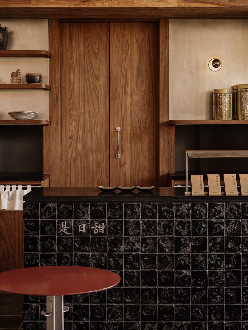 Service counter clad in black glazed tiles with timber cabinetry and shelving above