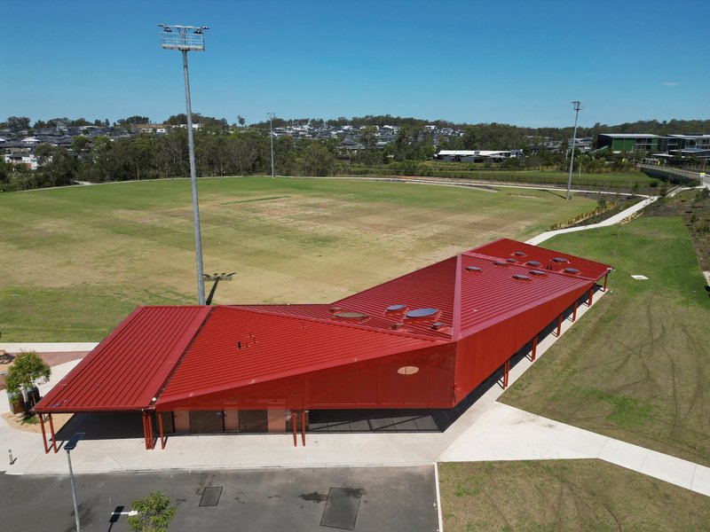 Aerial view of the angular red metal roof with service penetrations beside the oval field
