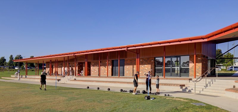 Covered veranda with slender steel columns and tiered concrete seating overlooking the playing field