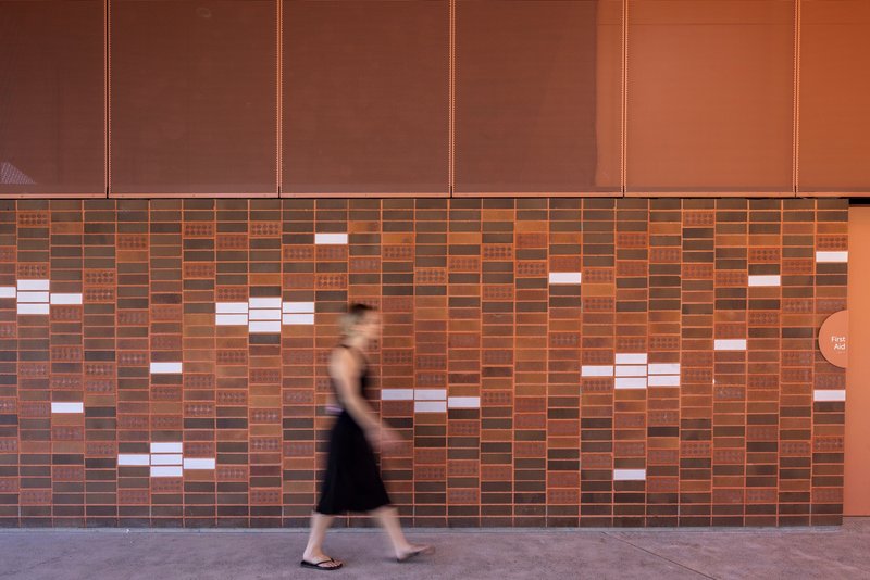Patterned brick wall with scattered white ceramic tiles as a person walks past in motion blur