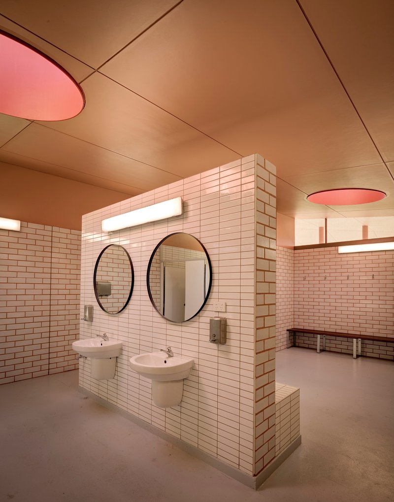 Freestanding tiled washbasin wall with round mirrors beneath pink ceiling light fixtures