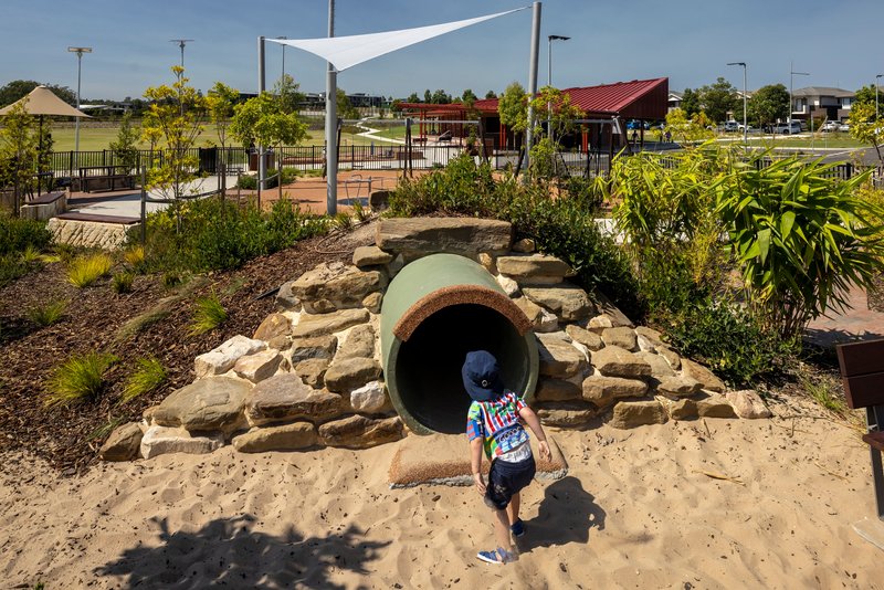Concrete tunnel entrance surrounded by stacked sandstone boulders and native planting with a child approaching