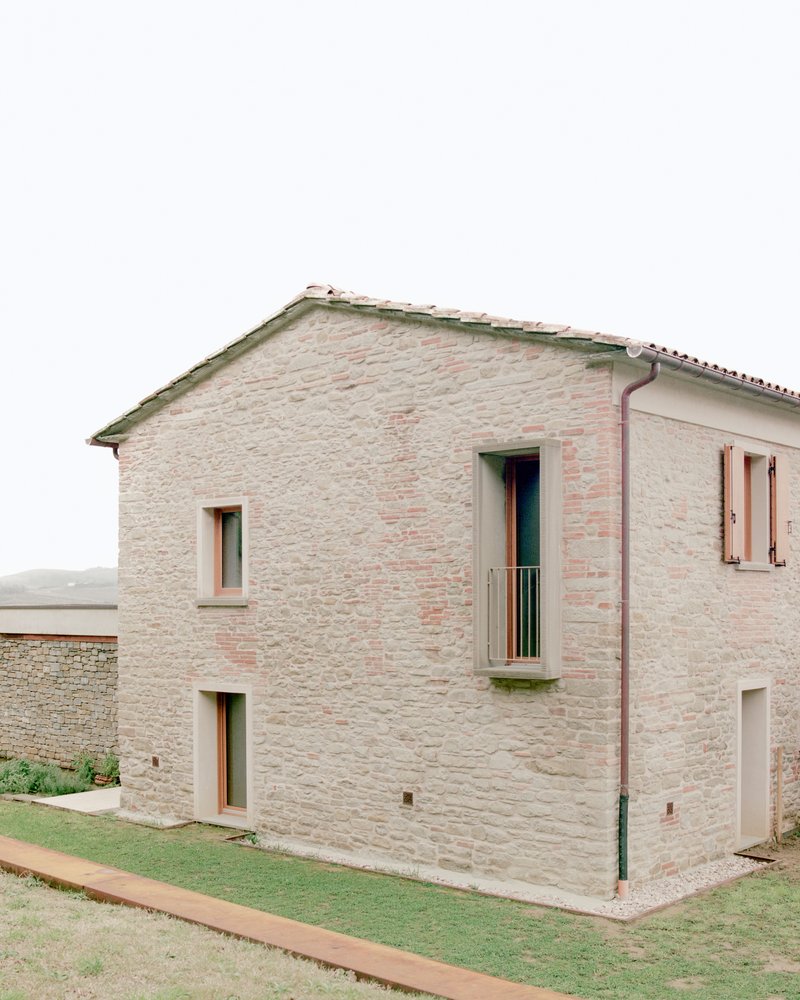 Two-storey stone facade with narrow windows and a small balcony beneath a tiled roof