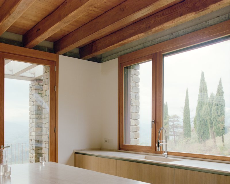 Kitchen counter with timber base units below windows framing cypress trees in misty landscape beyond