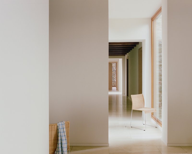Corridor view through white walls and doorways revealing stone column and wicker chair in daylight