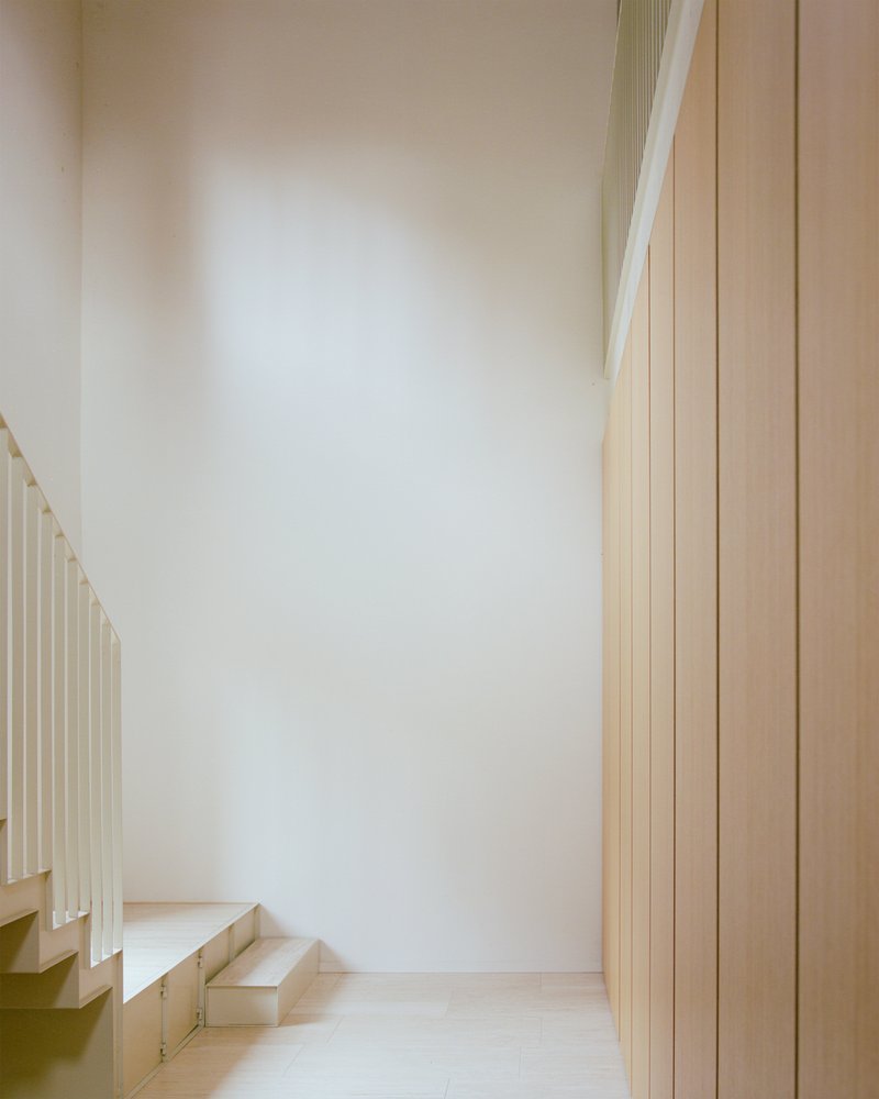 Stairwell with pale stone steps ascending past vertical wood paneling and white plaster walls