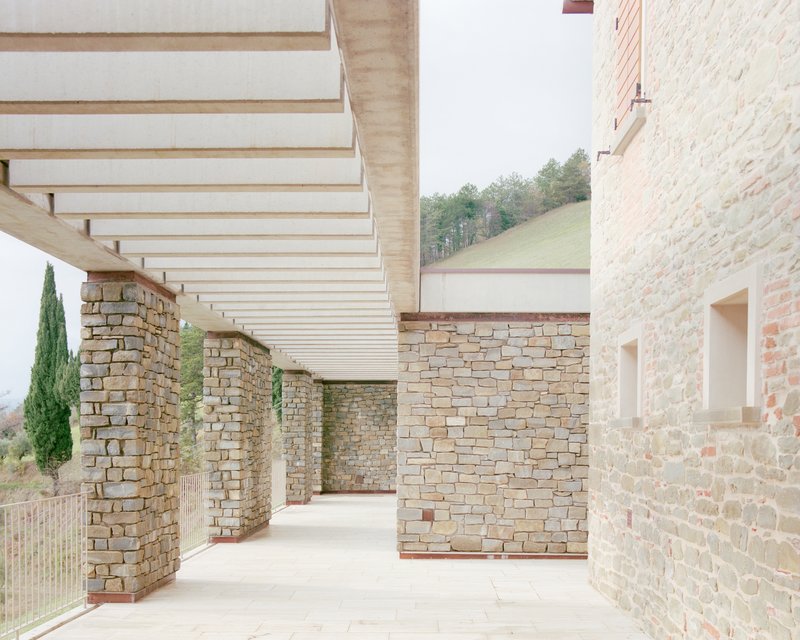 Covered terrace with stone columns and timber battens overlooking the hillside landscape