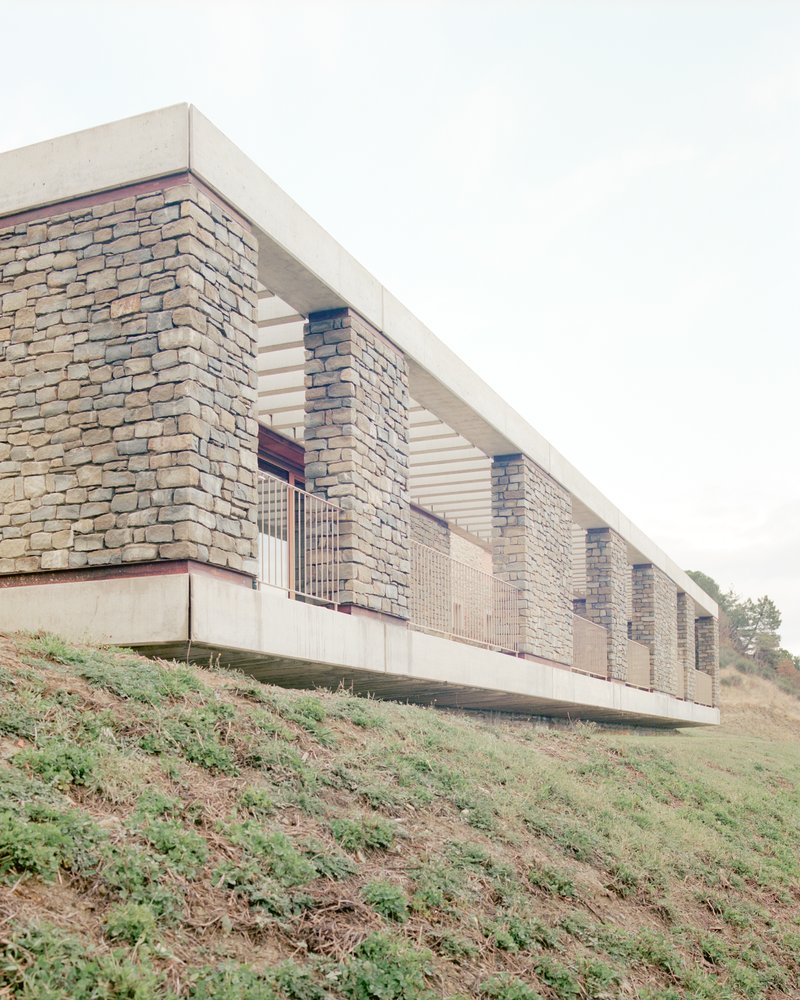 Side view of the elevated structure with stacked stone columns and concrete soffit above sloping terrain
