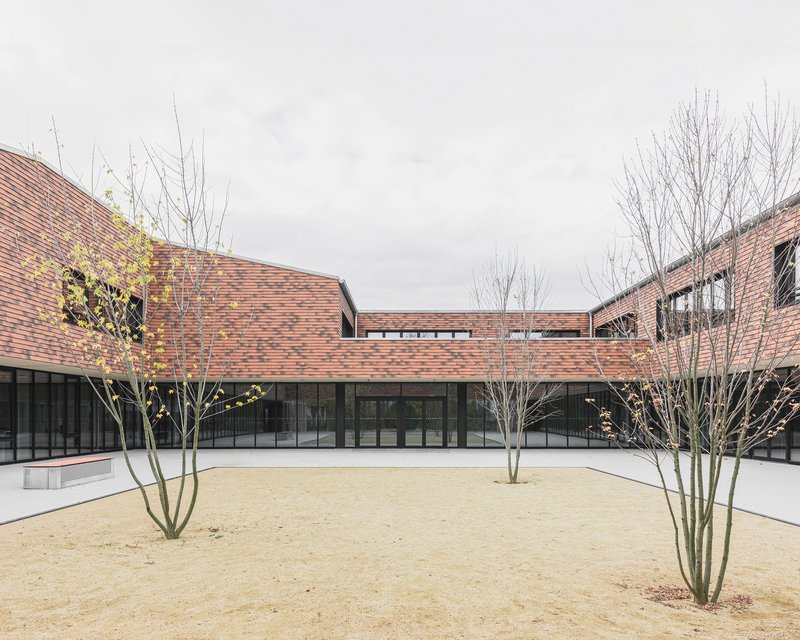 Interior courtyard with gravel surface and bare trees flanking a glazed corridor beneath pink brick volumes