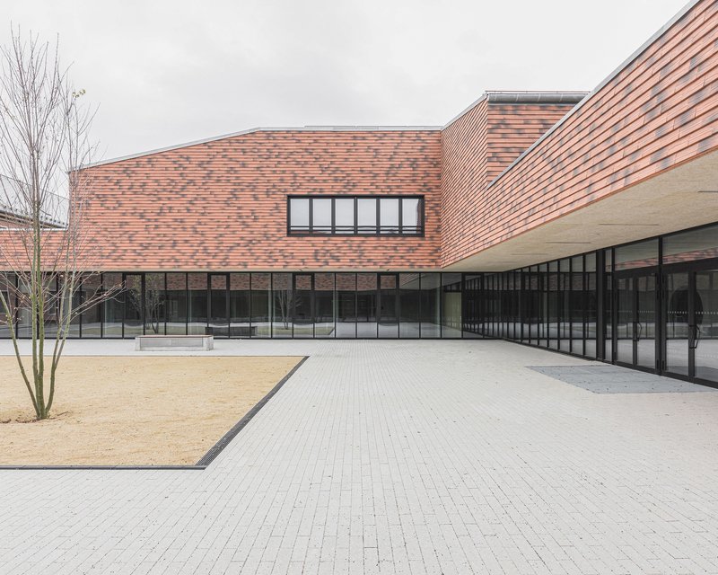 Paved courtyard with gravel bed and bare trees beneath pink brick facades and black-framed glazing