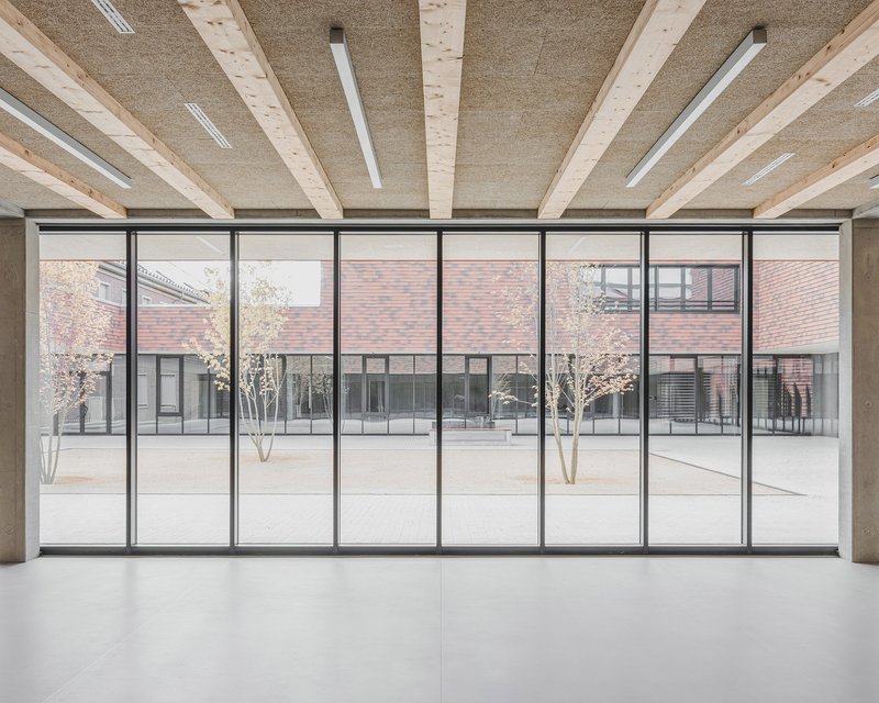 Interior gallery with timber ceiling beams overlooking a courtyard through floor-to-ceiling steel-framed glazing