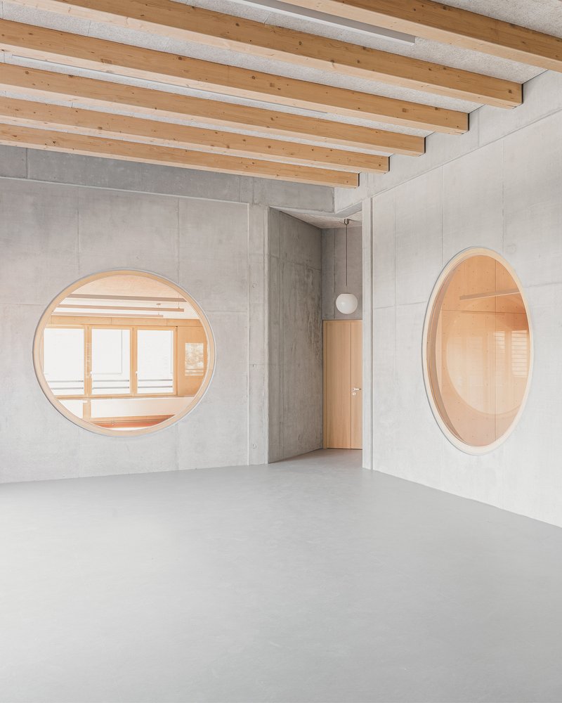 Polished concrete floor beneath exposed timber beams with circular windows framing adjacent rooms