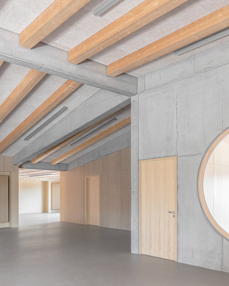 Junction of exposed timber ceiling beams meeting concrete walls with timber doors and partial circular window