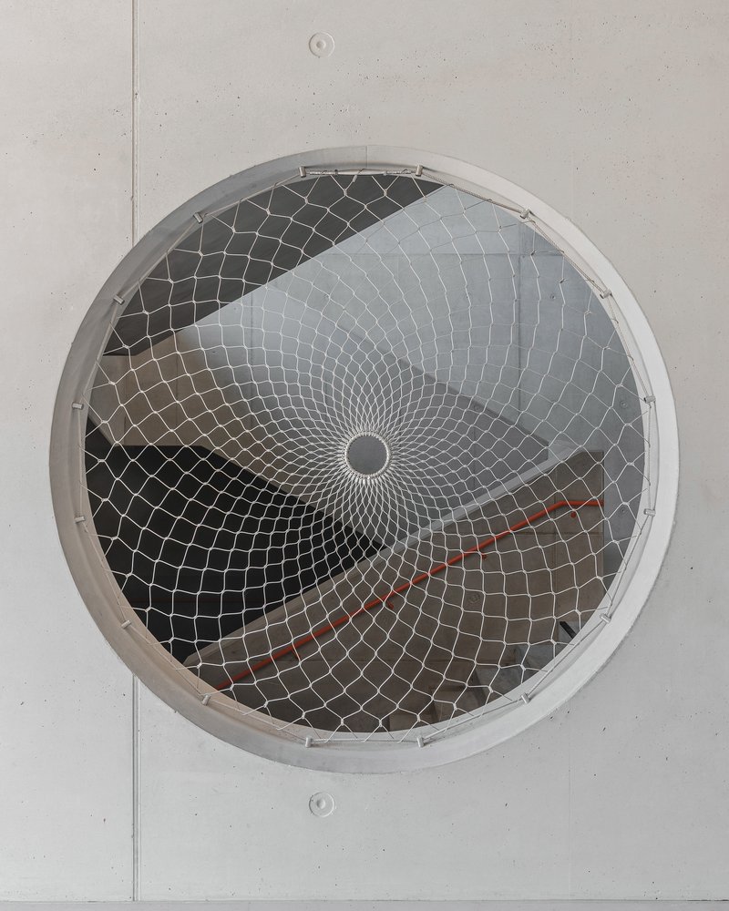 Circular ceiling vent with spiraling metal mesh guard in a light grey panel