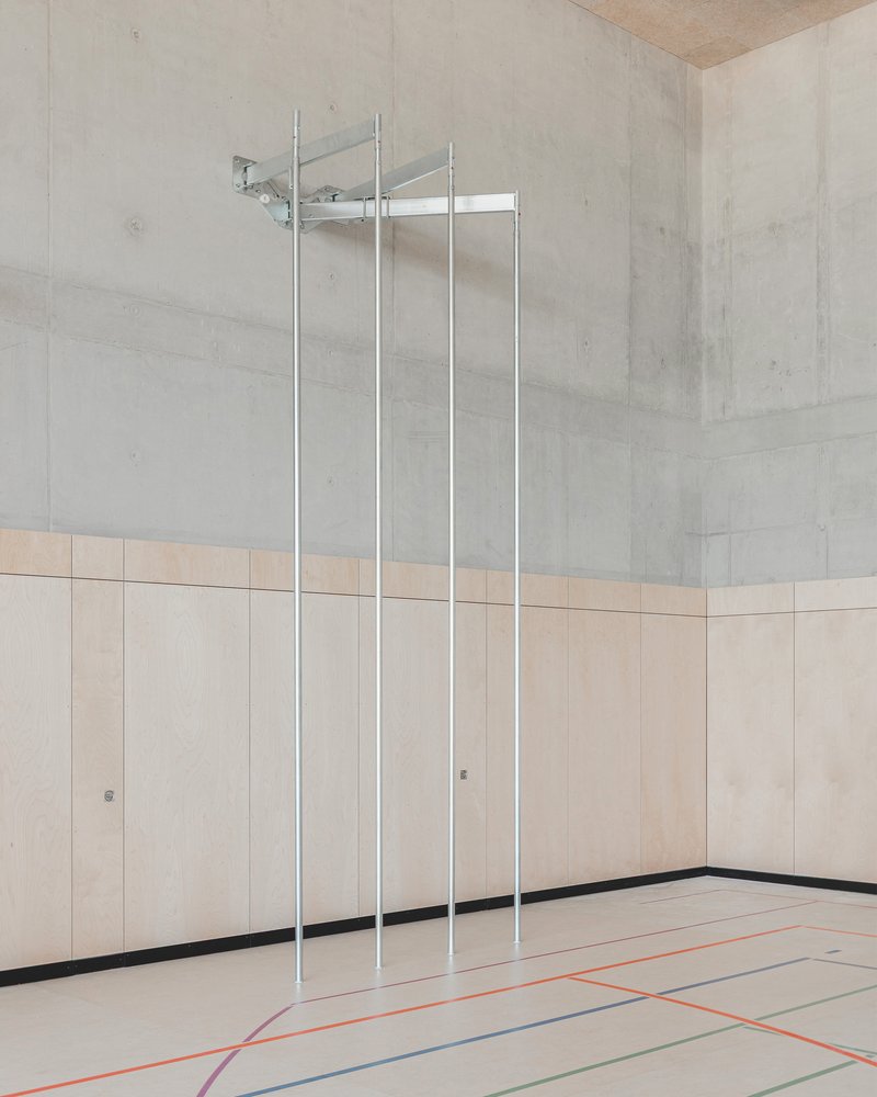 Interior gymnasium with pale timber wall panels and chrome poles hanging from exposed concrete ceiling