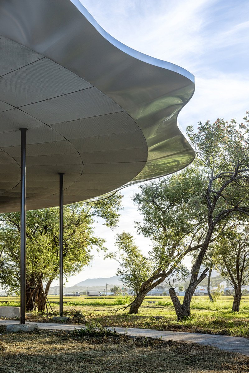Underside view of the rippling metal roof edge supported by columns among mature trees at dusk