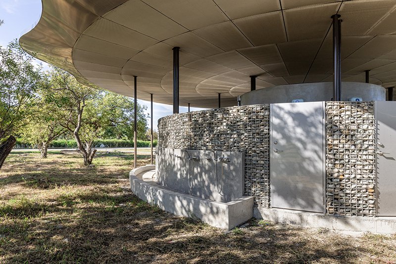 Concrete service core with gabion basket screens and metal door under the paneled canopy