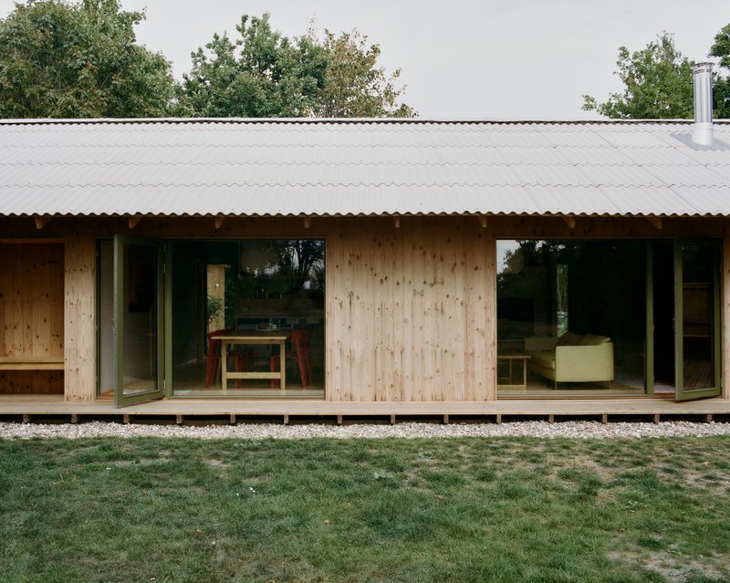 Light timber facade with sliding glass doors and corrugated metal roof above a gravel bed