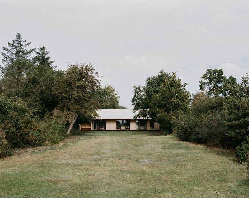 Low horizontal volume with flat roof nestled among mature trees on a mown grass lawn