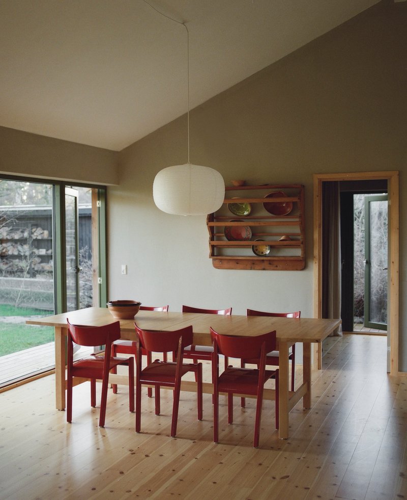 Dining area with red chairs around timber table beneath a paper pendant light