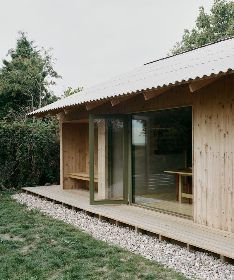 Covered timber deck with built-in bench and sliding doors under corrugated metal eave