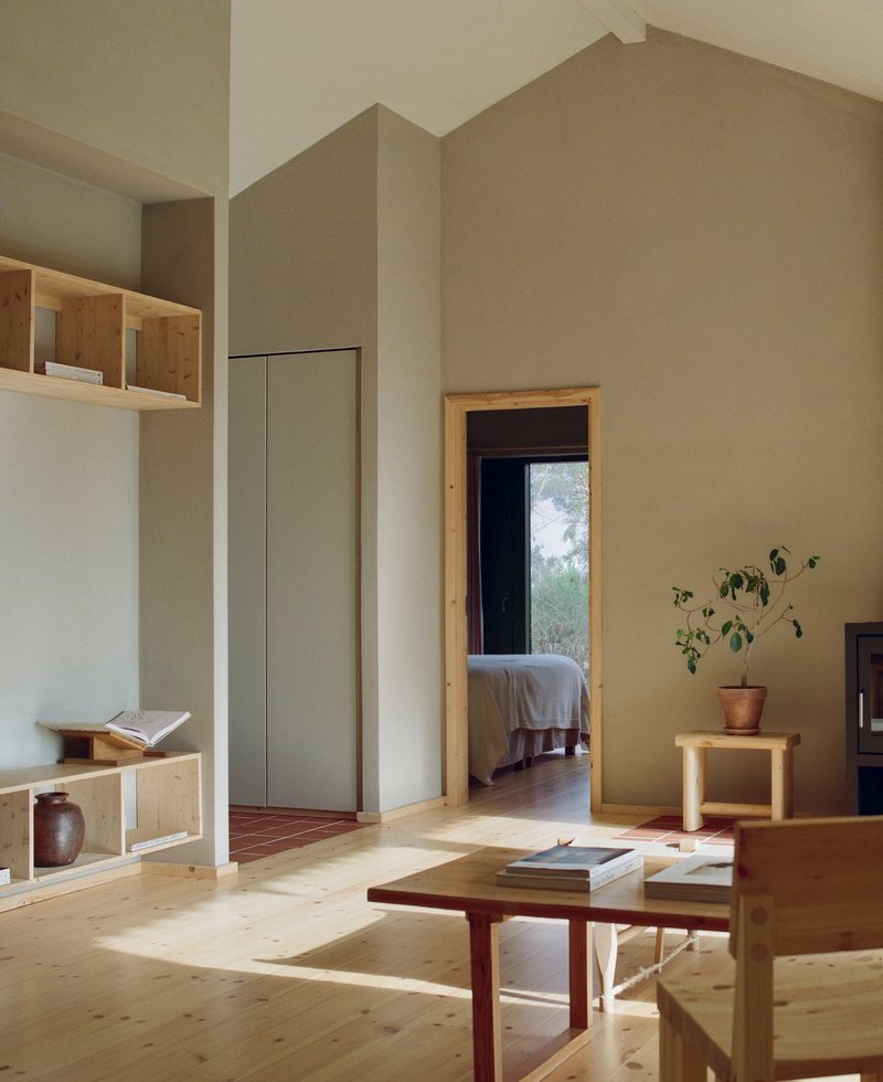Living room with pale plaster walls and timber joinery looking through a doorway to a bedroom