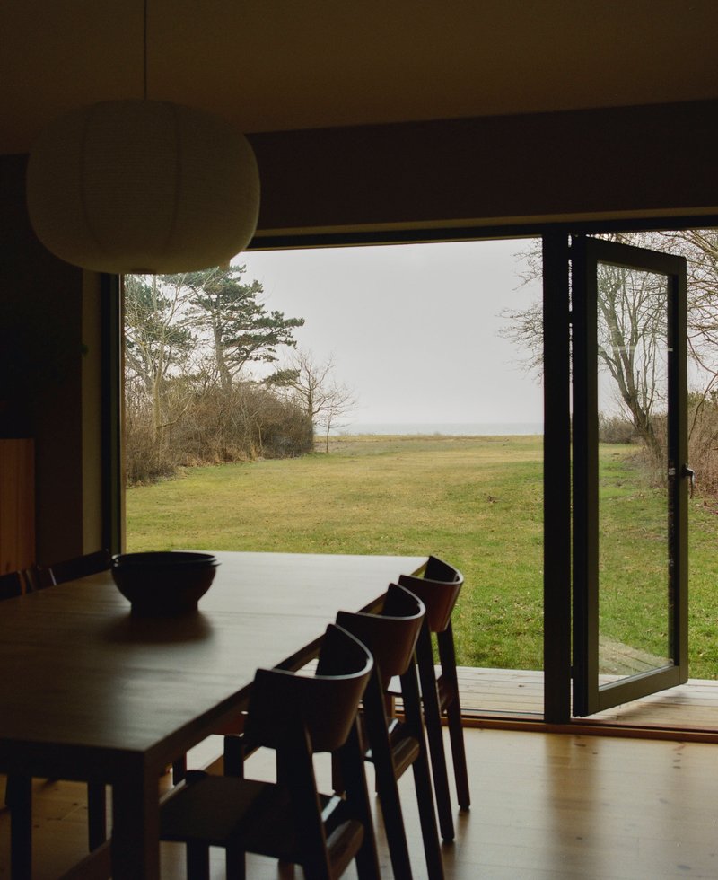 Dining table and chairs framing an open glazed door to the grassy field beyond