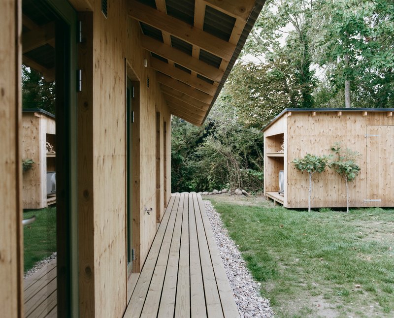 Timber deck connecting two pale wood pavilions beneath a cantilevered eave and surrounding trees