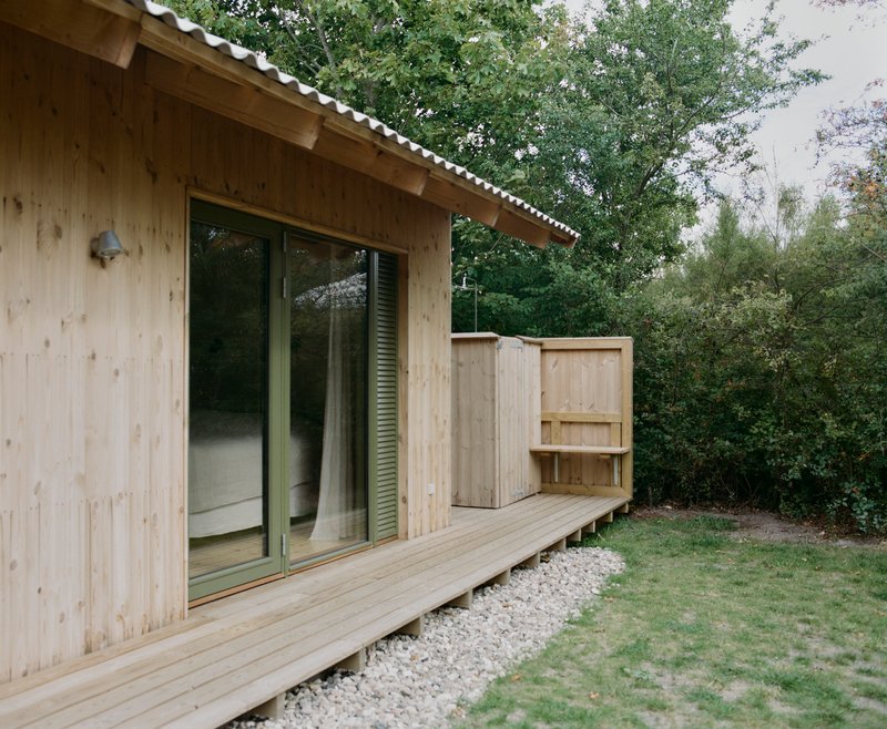 Exterior view of timber-clad volume with corrugated metal roof and sliding glass doors to deck