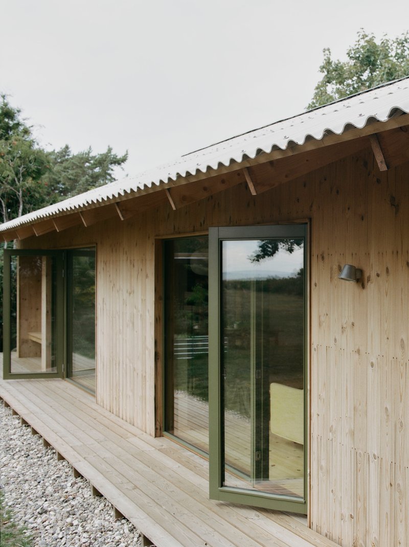 Facade showing vertical timber cladding with dark-framed glazing beneath a scalloped metal roof