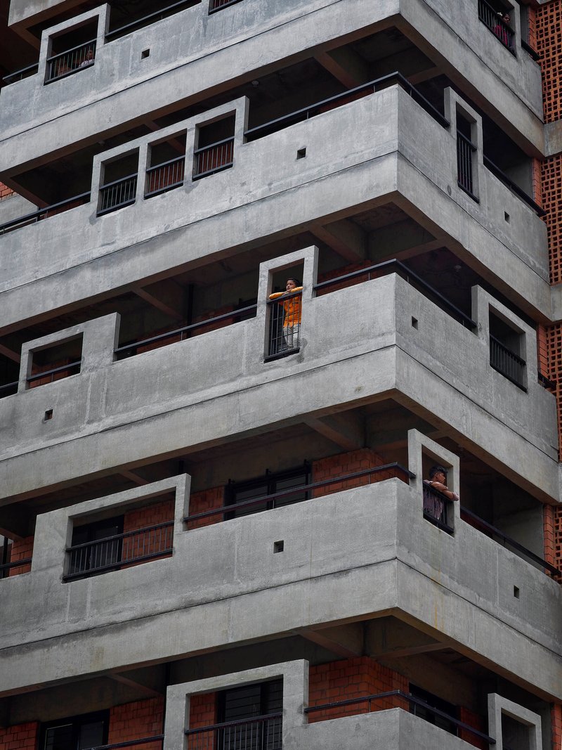 Stacked concrete balconies with deep recesses and a resident visible in one window opening