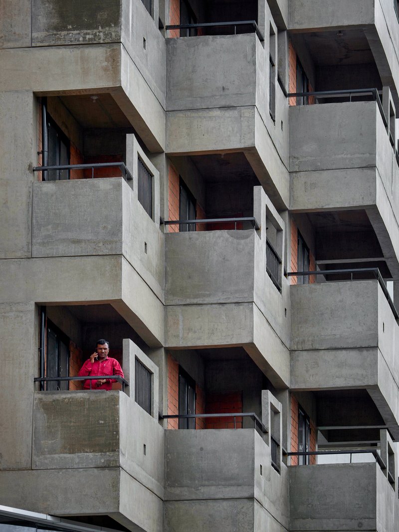 Concrete balconies with metal railings and exposed brick walls where a resident in red stands looking out