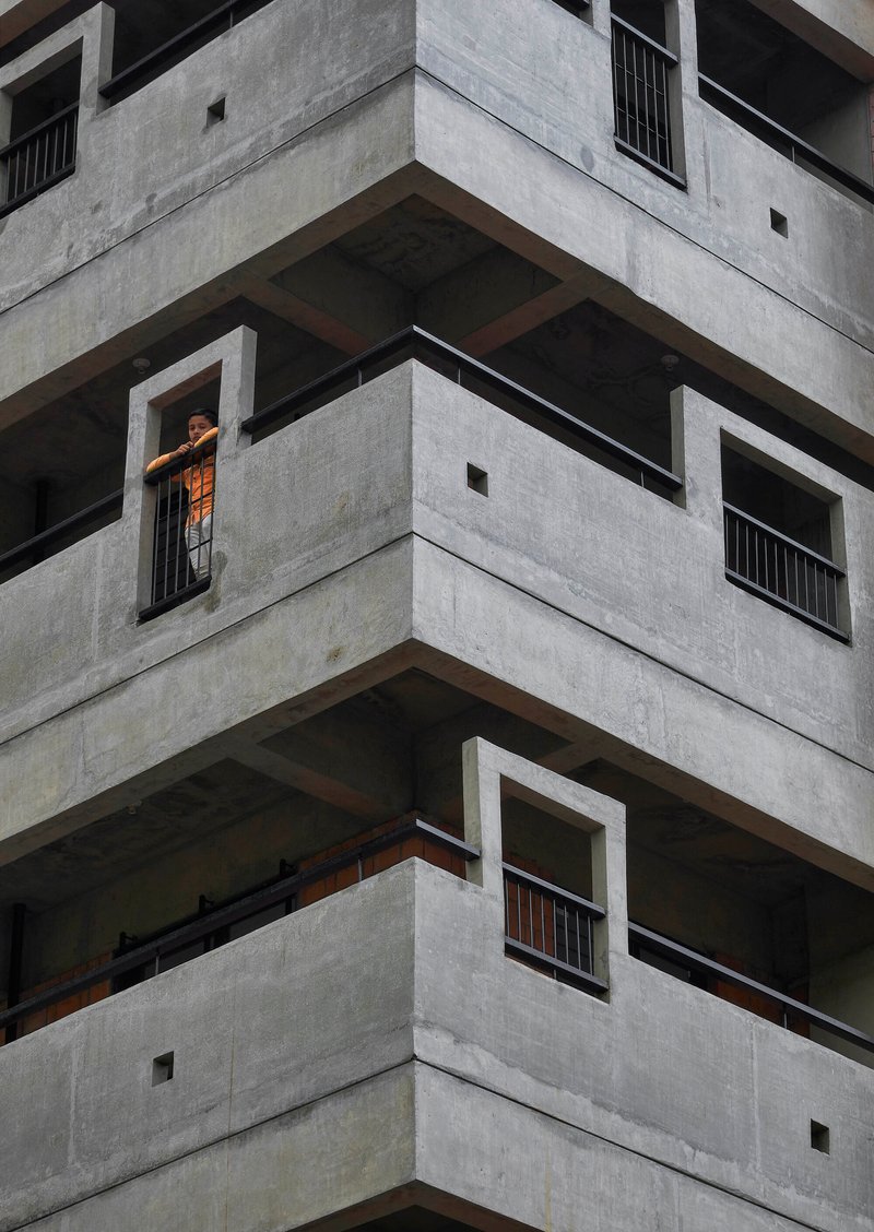 Corner detail of stacked concrete balconies with deep recesses and a resident in the window