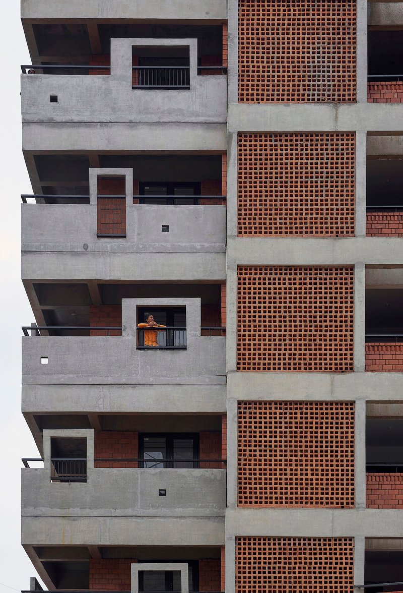 Stacked concrete balconies with terracotta brick panels where one resident leans on a railing