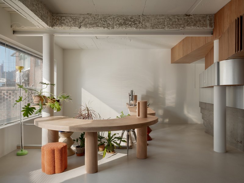 Workspace with sculptural timber table and potted plants in afternoon sunlight beneath exposed concrete beam