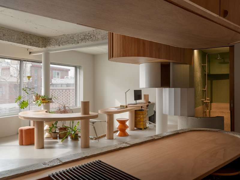 Living area with rounded table and curved wood desk platform overlooking a tiled bathroom in afternoon light
