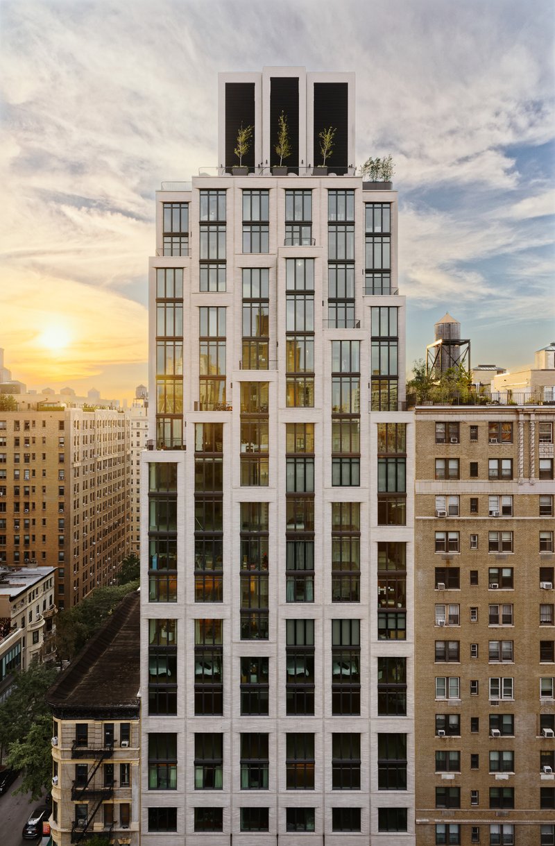 Full facade view showing the white frame grid with three dark rooftop volumes and planted terraces