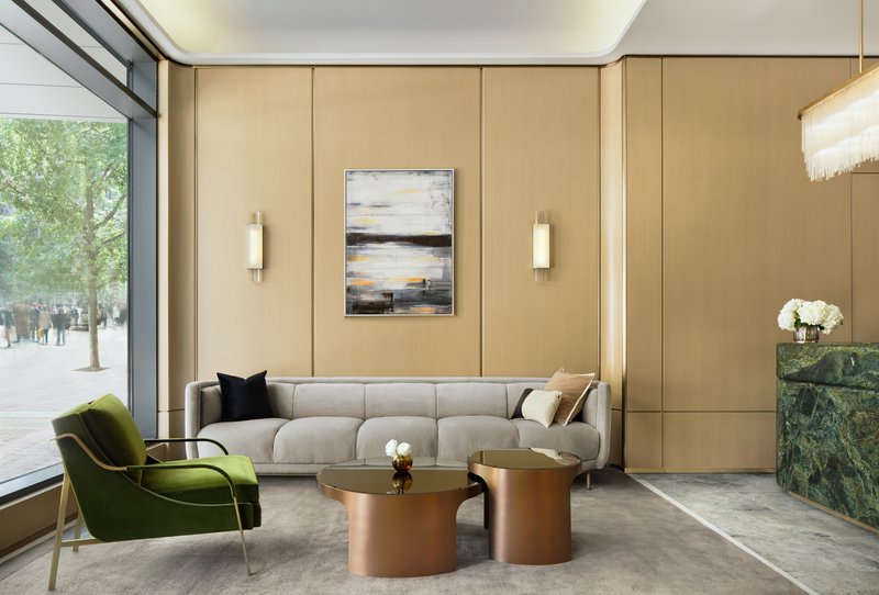 Lobby seating area with beige paneled walls, a corner window overlooking street trees, and copper tables