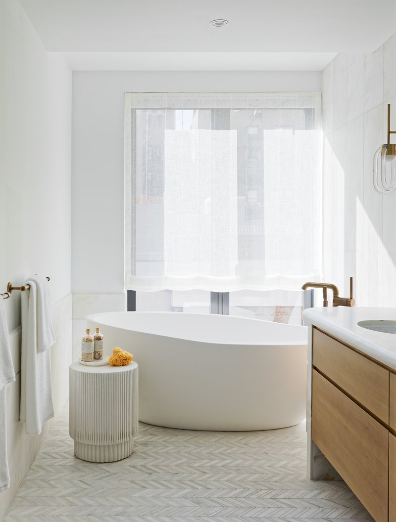 Bathroom with freestanding white tub and herringbone floor tile near a bright window
