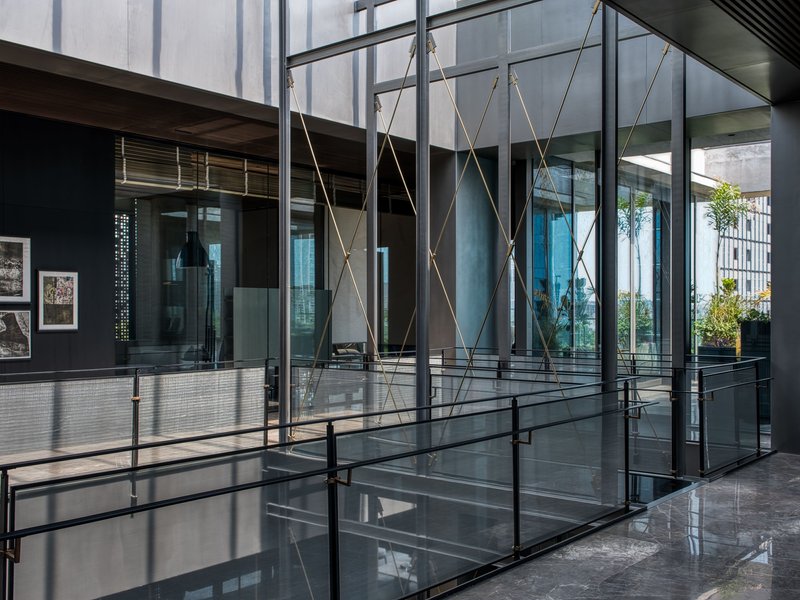 Glass-enclosed atrium with suspended rope bracing and steel walkways connecting interior volumes under overcast skies