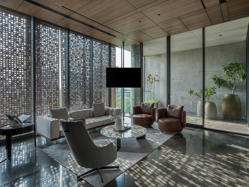 Double-height living space with perforated terracotta screen wall casting dappled shadows across polished stone floor