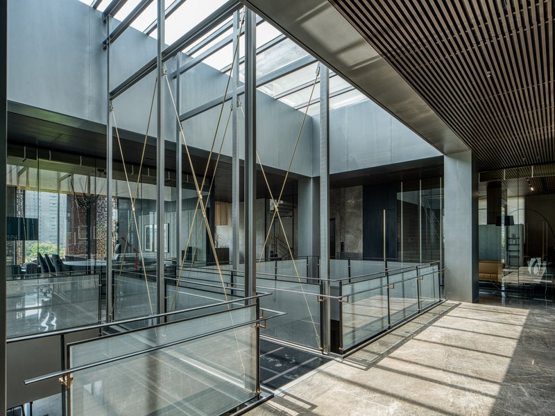 Glass-enclosed bridge with brass tension cables crossing an interior courtyard under a translucent skylight