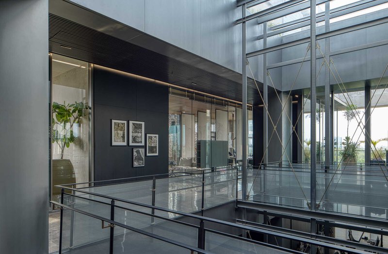 Interior walkway with glass railings and brass cable structure overlooking dark paneled walls and hanging plants