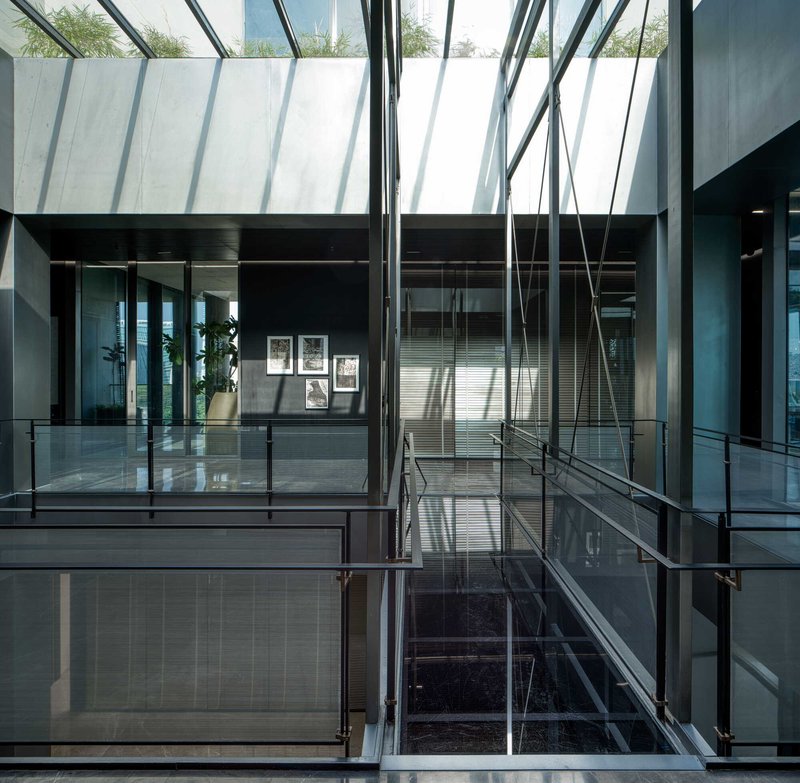 Glass-enclosed stairwell beneath angled skylight with steel structural cross-bracing and reflection in polished floor