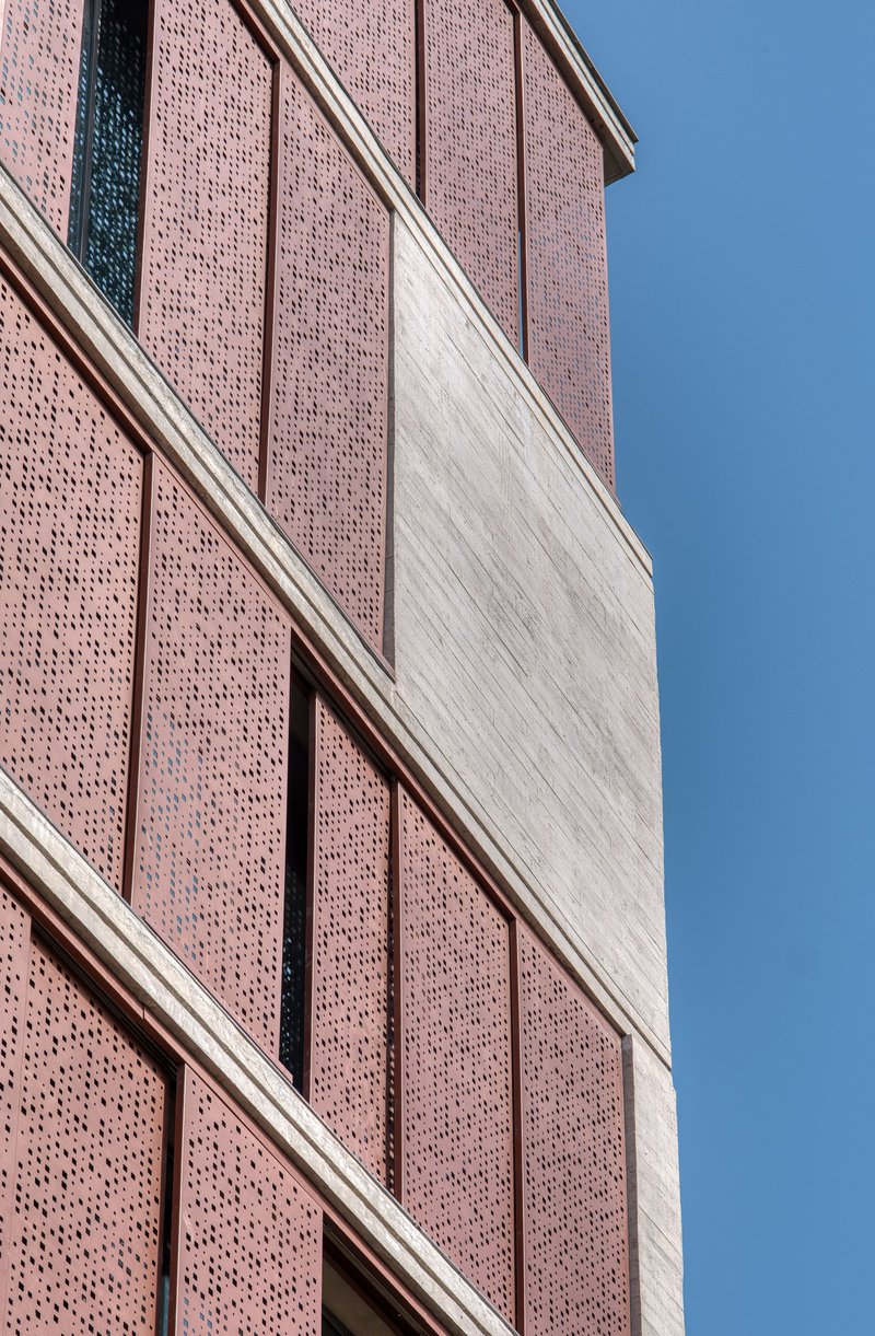Close-up of perforated brick panels alternating with vertical concrete bands under clear blue sky