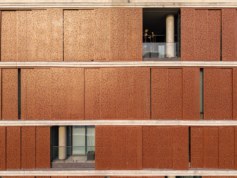 Front elevation of perforated brick facade with horizontal concrete bands and recessed balconies in warm light