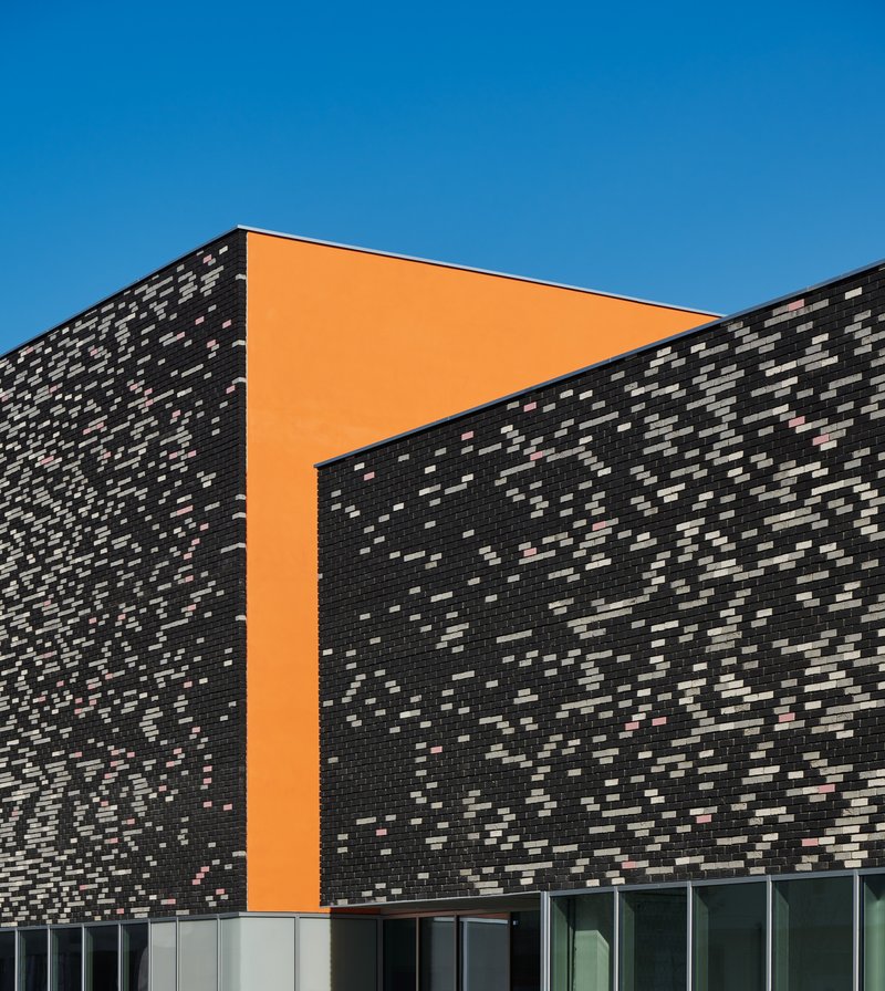 Corner detail of the speckled dark brick wall with orange panel insert framing the glazed base