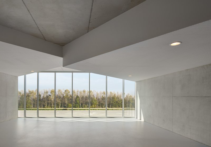 Interior room with concrete walls and ribbed ceiling opening to glazed facade overlooking trees