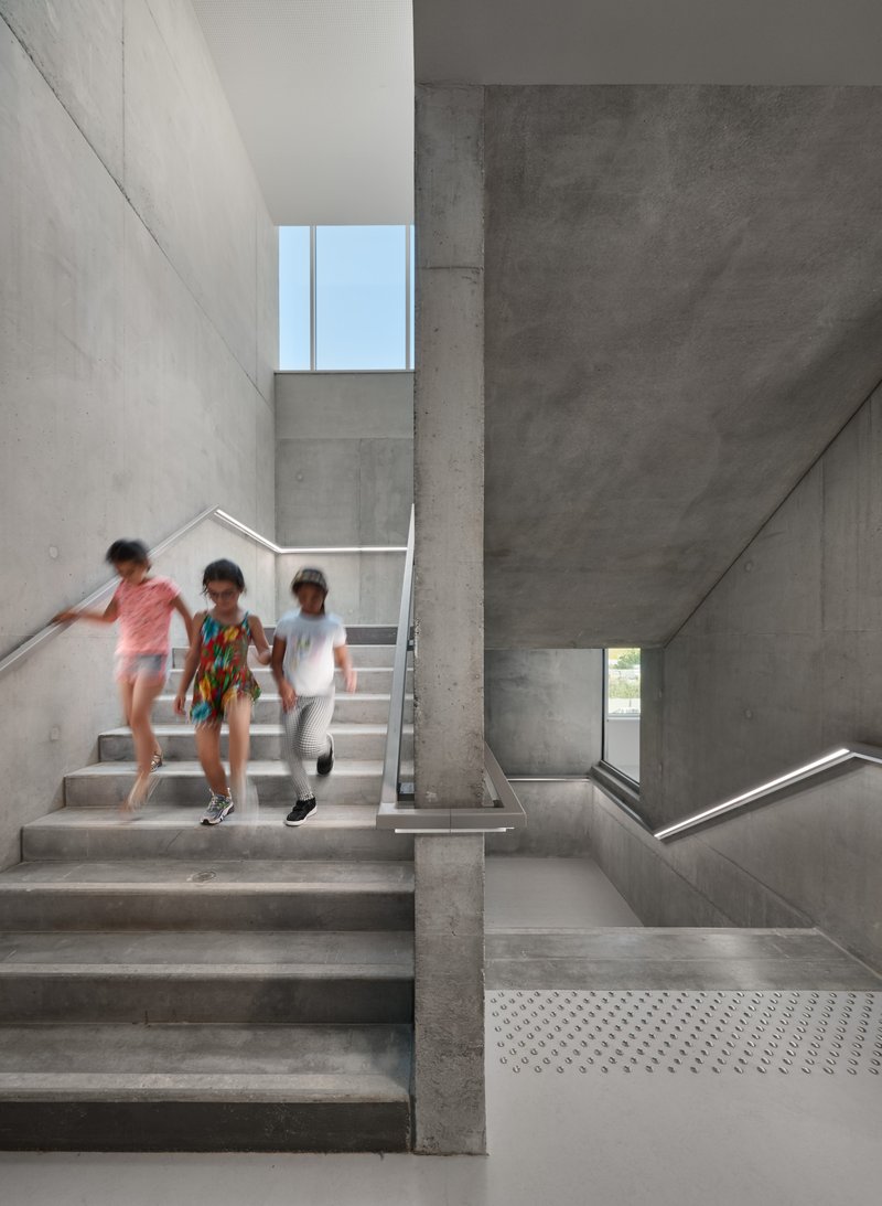 Concrete stairwell with three children descending the steps beneath a skylight window